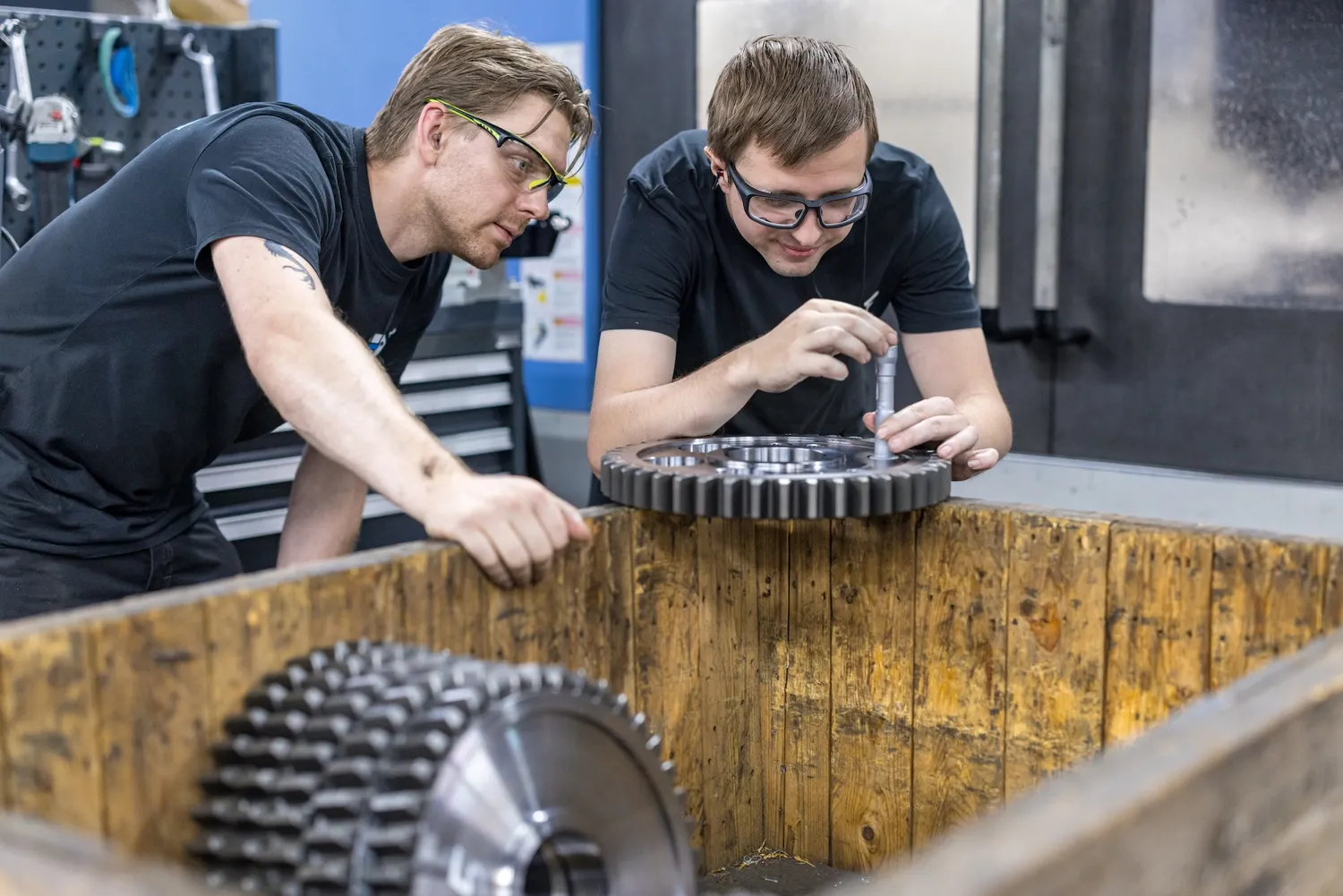 Samen een tandwiel controleren Twee medewerkers controleren een tandwiel bij een houten kist
