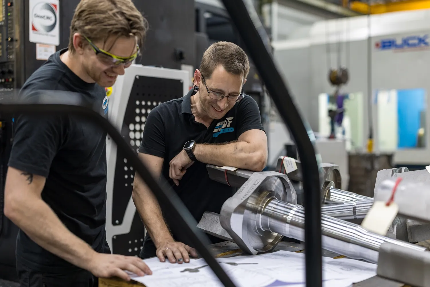 Overleg over een tekening Twee collega's bespreken een technische tekening bij de machine