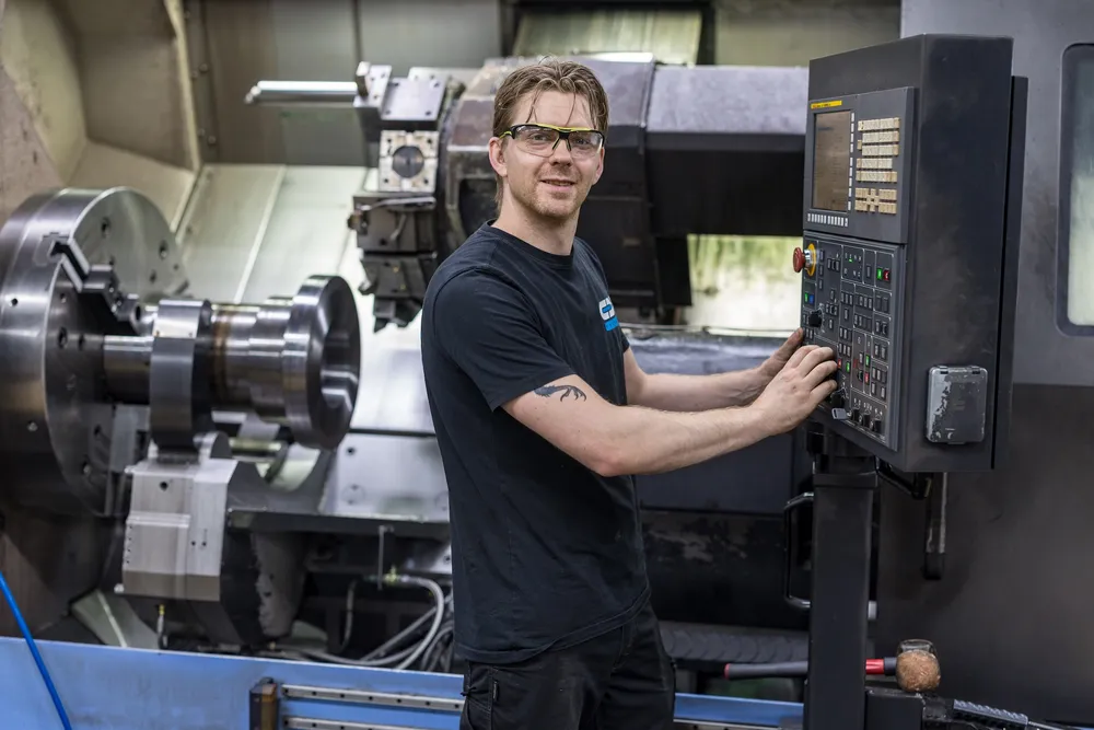 CNC verspaner Lachende medewerker bij het bedieningspaneel van een CNC draaibank